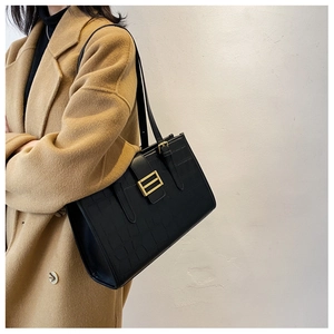 Detail of a black stone-textured tote with a gold H-buckle worn on a camel coat