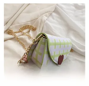 Detail showing green plaid saddle bag with brown heart motif and golden chain strap