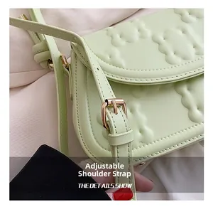 Detail of adjustable shoulder strap and textured embossed pattern on green crossbody bag