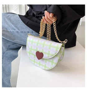 Detailed close-up of green gingham saddle bag with a red heart and gold chain strap