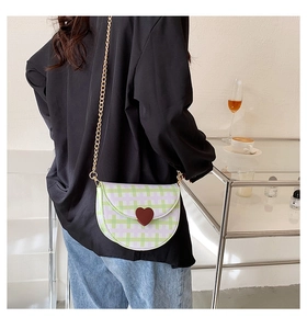 Detail of plaid saddle bag with heart charm and golden chain strap on a model