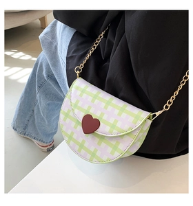 Detail of green plaid saddle bag with heart buckle and gold chain strap shown on model