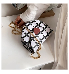 Detail of checkered saddle bag with red heart lock and golden chain strap on table