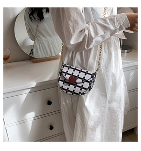 Detail of plaid saddle bag with red heart clasp and gold chain on white dress