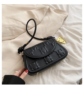Close-up of black crossbody bag with quilted pattern and gold cheese pendant detail