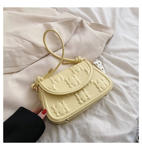 Detail of pale yellow biscuit shoulder bag with embossed texture on soft white fabric