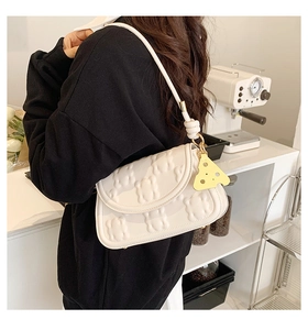 Detail of cream white underarm bag with 3D bear embossing and yellow cheese pendant