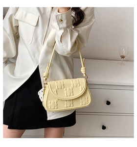 Pale yellow underarm bag with quilted wave texture and a cheese charm on a model