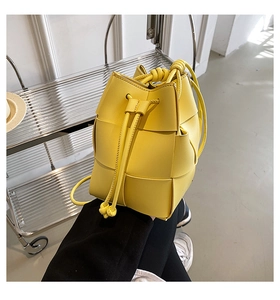 Detail of yellow woven leather bucket bag with drawstring closure and slim shoulder strap