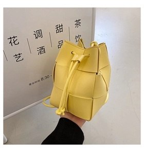 Close-up of lemon yellow hand-woven leather bucket bag featuring signature wide strap weaving