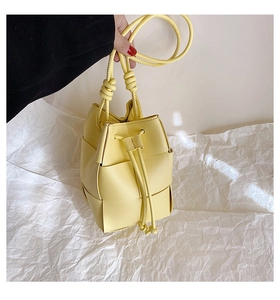 Detail of a bright yellow woven bucket bag with leather drawstring and knot detail