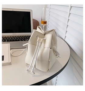 Close-up of beige woven bucket bag with drawstring closure and slim shoulder strap