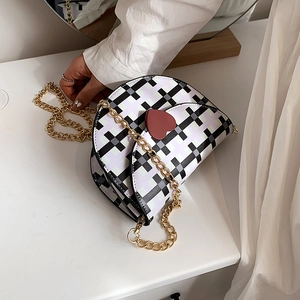 Checkered saddle bag with heart charm and gold chain strap on a white table