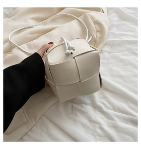 Detail of white woven bucket bag showing wide leather texture and crossbody strap