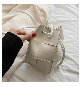 Detail of cream woven bucket bag showing textured wide-weave design and drawstring closure