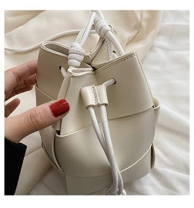 Close-up of cream woven bucket bag featuring large grid leather texture and drawstring