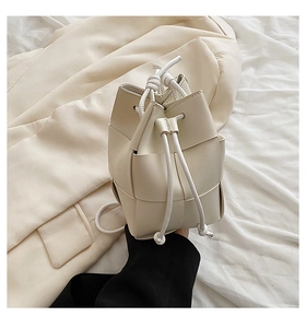 Detail of hand-woven cream bucket bag with drawstring closure on beige blazer
