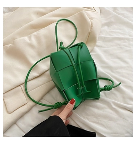 Detail of green woven leather bucket bag featuring knot drawstring on white fabric