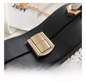Detail view of a black leather handbag with a gold metal clasp and silver rhinestone fringe