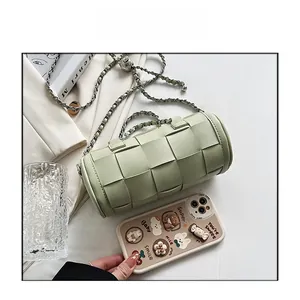 Detail view of a light green woven cylinder bag with chain strap against daily items