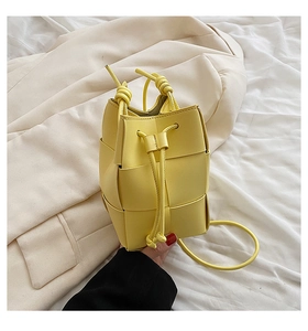 Close-up of bright yellow woven bucket bag with leather texture and drawstring detail