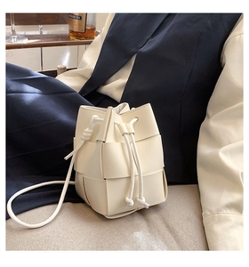 Detailed view of cream woven leather bucket bag with drawstring closure and slim strap