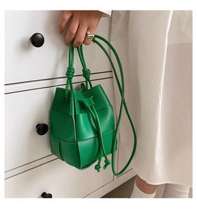 Close-up of bright green woven leather bucket bag with drawstring knot and fine straps