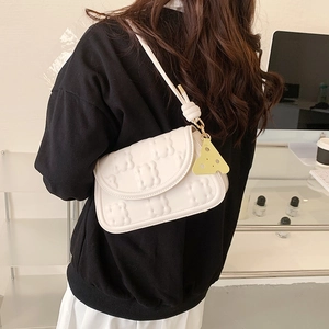 White textured shoulder bag with a yellow cheese charm worn across the back by a model