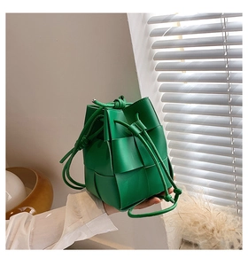Close-up of green woven bucket bag with leather straps in a bright interior setting
