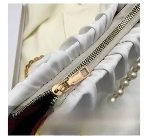 Détail de la fermeture dorée sur sac plissé blanc avec bandoulière perle et doublure