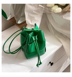 Detail view of vibrant green woven bucket bag with intricate leather weaving and drawstring