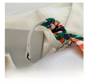 Detail of cream handbag featuring embossed cartoon patterns and silk scarf handle wrap