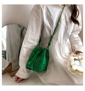 Detailed close-up of a vibrant green hand-woven bucket bag on a white dress