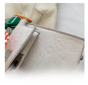 Detail of embossed beige leather bag featuring heart patterns and silk scarf handle