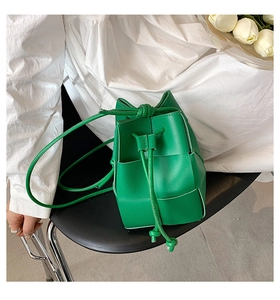 Close-up of vibrant green hand-woven bucket bag with drawstring and leather texture