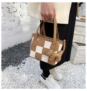 Détail du sac seau tressé à damier marron et blanc avec pendentif chien et bandoulière