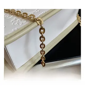 Detail of white embossed leather bag featuring gold chain strap and floral textures