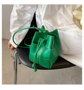Detail of green woven leather bucket bag featuring drawstring closure and textured finish