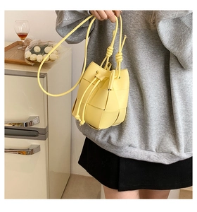 Close-up of lemon yellow woven bucket bag with drawstring closure and slim strap