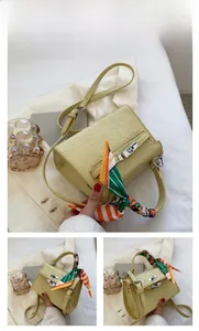 Detail of yellow embossed crossbody bag featuring a silk scarf wrapped handle and metal clasp