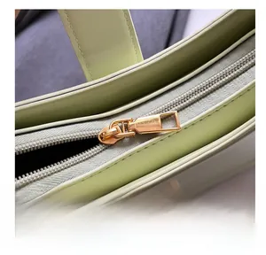 Detailed close-up of premium gold metal zipper and stitching on light green leather bag