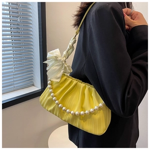 Détail du sac plissé jaune avec chaîne de perles et grand nœud en satin blanc