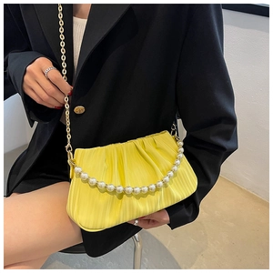 Détail d'un sac jaune plissé avec poignée en perles et chaîne dorée sur veste noire