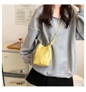 Detail of yellow woven bucket bag with thick leather strips and drawstring closure