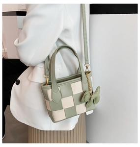 Détail du sac seau tissé vert et crème avec breloque nœud porté sur un costume blanc