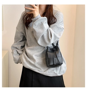 Detail of a black woven crossbody bucket bag with drawstring closure for casual outfit