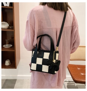Détail du sac seau à damier avec texture en cuir et accessoire suspendu de dessin animé