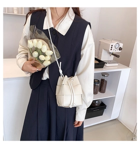 Detail of white woven leather bucket bag with drawstring closure and slim shoulder strap