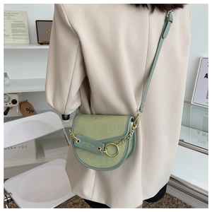 Detail of light green crocodile embossed saddle bag with gold chain on model shoulder