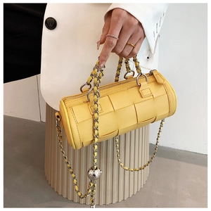 Close-up of yellow woven cylinder bag with chunky silver chain and metal ball charm